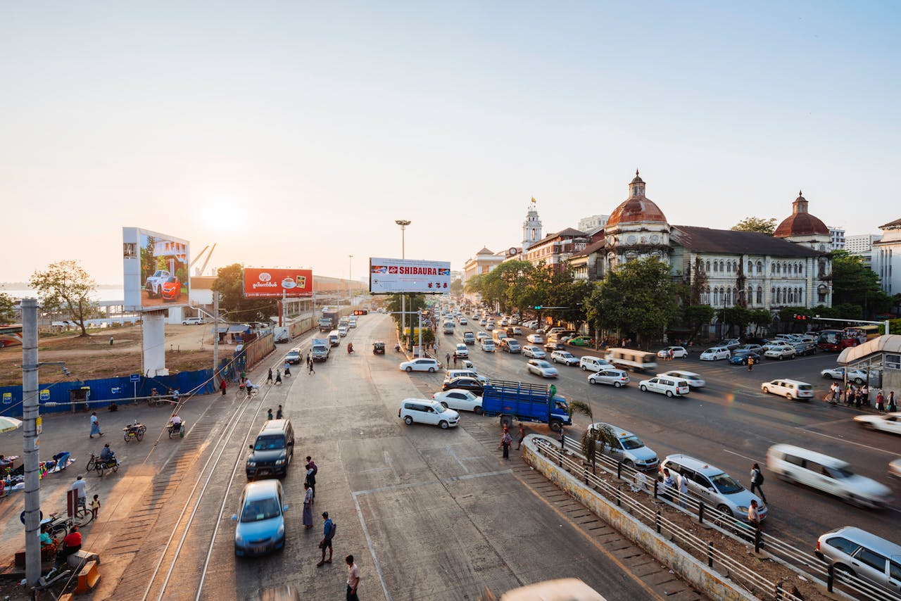 discover A vibrant urban intersection in Yangon, Myanmar, at sunset with vehicles and pedestrians.